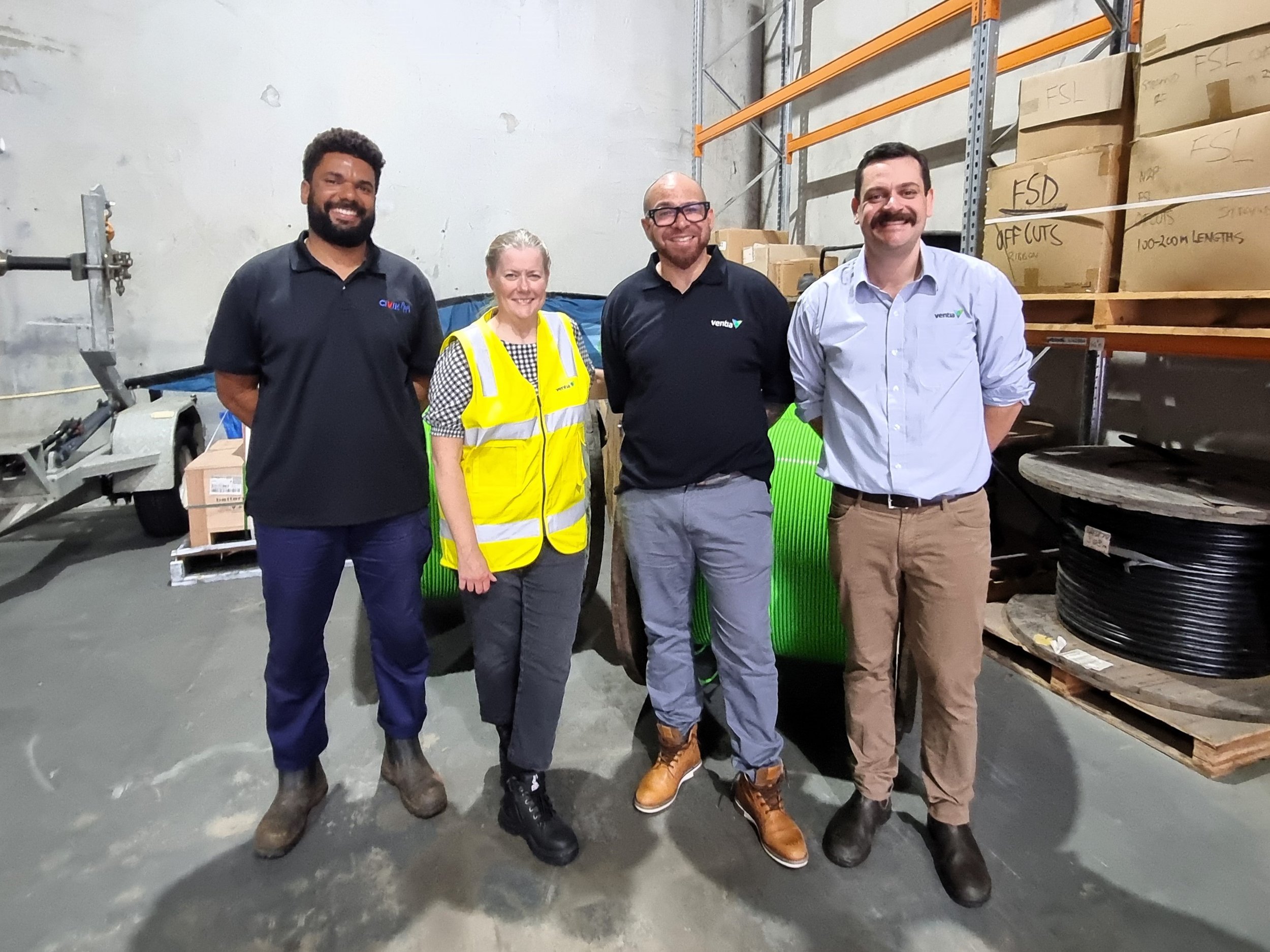 Four people stand in front of green NBN cable in a warehouse